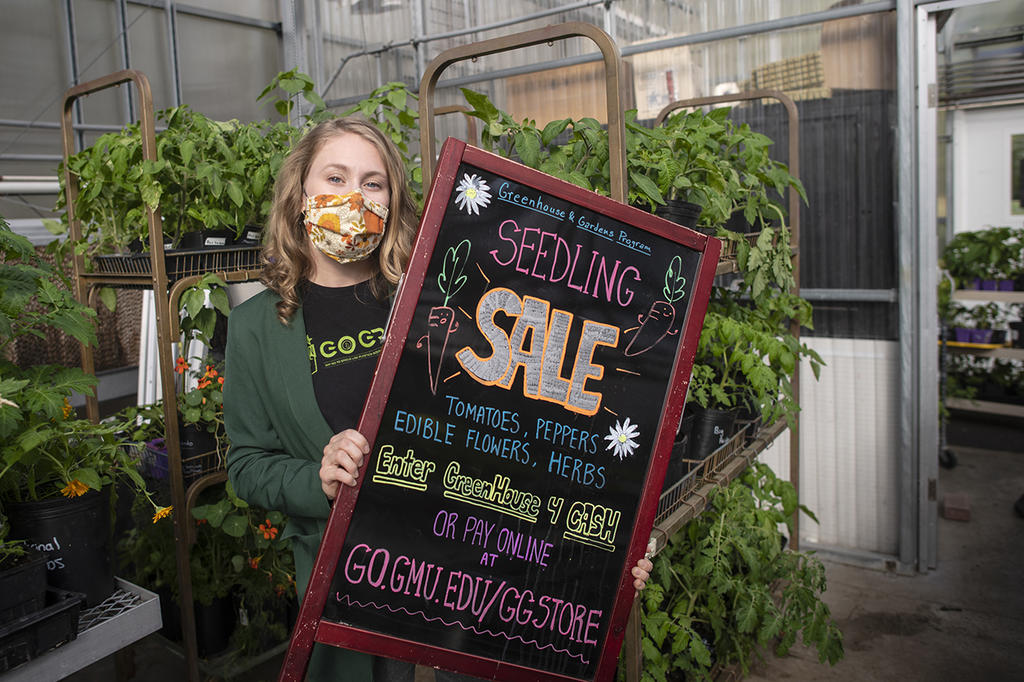 Blonde female student holding a promotional chalkboard in a plant nursery